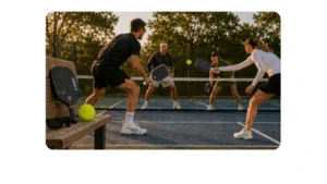 Four pickleball players engaged in a kitchen-line rally with featured paddles and gear courtside during golden hour.