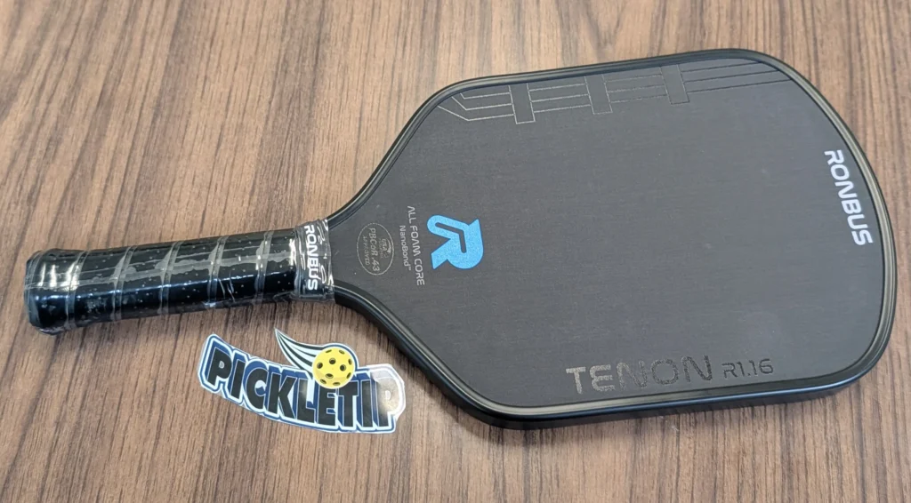 Ronbus Tenon R1.16 pickleball paddle on a wooden table with a PickleTip sticker beside it